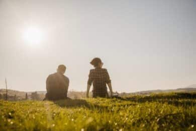 Two people sitting on grass, enjoying the sunlight in a serene outdoor setting.