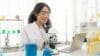 A woman in a lab coat examines a microscope, representing her role as an online chemistry tutor.
