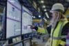 A woman in a hard hat and yellow vest examines a computer screen, focusing on technical assessments in industrial practices.