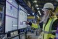 A woman in a hard hat and yellow vest examines a computer screen, focusing on technical assessments in industrial practices.