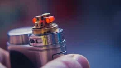 A hand gripping a lighter, with prefilled pods placed nearby, suggesting a vaping context.