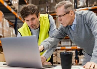Two men in a warehouse working together on a laptop related to customs clearance