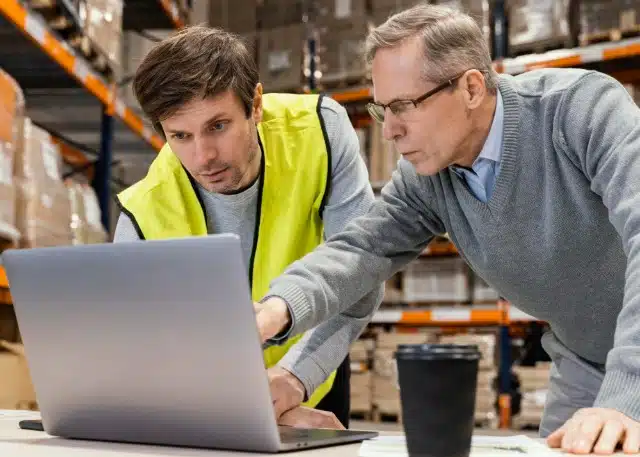 Two men in a warehouse working together on a laptop related to customs clearance