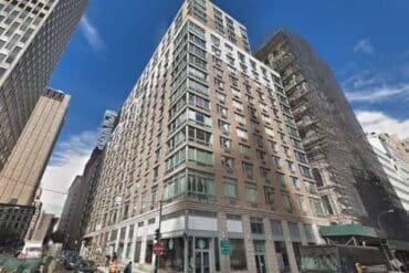 A high-rise building with many windows stands prominently on 111 Worth Street, reflecting city life.