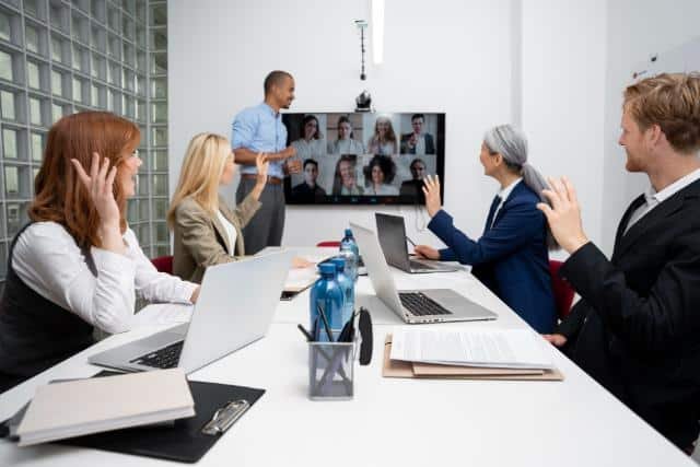 Business professionals in a meeting room using a laptop and a 360 conference camera for a video call.