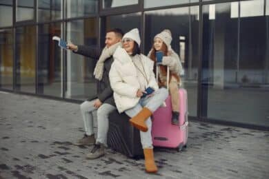 A family stands with luggage, including a pink suitcase, ready for travel with American Forces Travel.