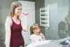 A woman and her young daughter happily brush their teeth together in a colorful bathroom, sharing a joyful routine.
