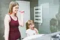 A woman and her young daughter happily brush their teeth together in a colorful bathroom, sharing a joyful routine.