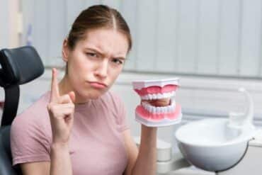 A woman smiling while holding a fake tooth model in front of her, demonstrating dental health education.