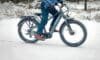 A man rides a bike through a snowy landscape, showcasing winter cycling in action.