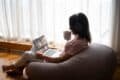 . A woman relaxes on a bean bag chair, wearing headphones and using a laptop, with "IYF TV" visible on the screen.