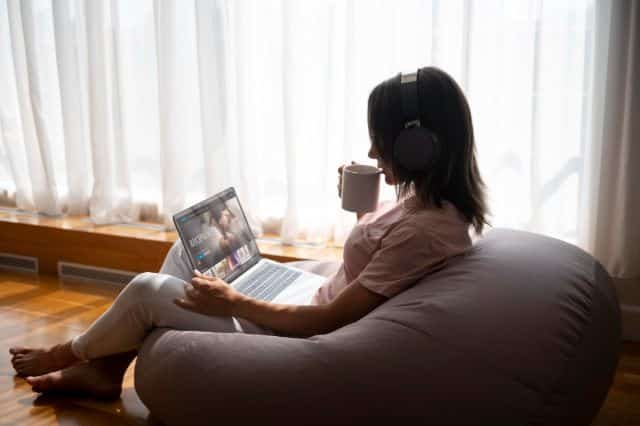 . A woman relaxes on a bean bag chair, wearing headphones and using a laptop, with "IYF TV" visible on the screen.
