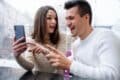 A man and woman laugh together while looking at a cell phone, enjoying content from Just For Fans videos.