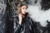 A woman in a leather jacket exhales vapor from an MR FOG.