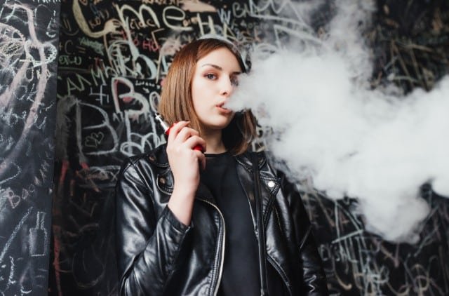 A woman in a leather jacket exhales vapor from an MR FOG.