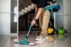 A man cleans a floor with a mop, working on home restoration after water damage.