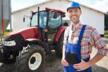 Smiling man in front of a tractor, representing a Tractor Supply Sales Associate role.