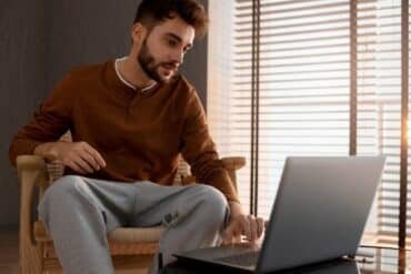 A man sitting on a chair, focused on his laptop while exploring the meaning and origin of Tsunaihaiya.
