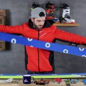 A man holds a pair of skis in front of a table with Zuschneidfelle, ready for winter sports preparation.