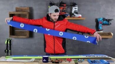 A man holds a pair of skis in front of a table with Zuschneidfelle, ready for winter sports preparation.