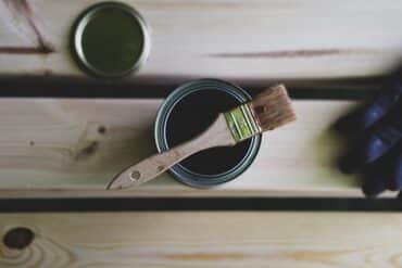 A paint can and a brush resting on a wooden table, ready for a creative project.