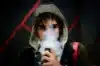 A man wearing a hoodie is smoking an electronic cigarette, specifically a Foger vape.
