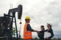Two men and a woman shake hands in front of an oil pump, symbolizing collaboration in offshore oil rig jobs.