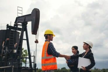 Two men and a woman shake hands in front of an oil pump, symbolizing collaboration in offshore oil rig jobs.