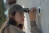 A woman wearing a cap looks directly at the camera, highlighting her involvement in security camera installation.
