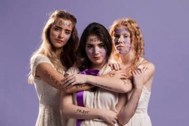 Three women with colorful face paint and names written on their arms, smiling and posing together.