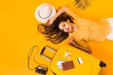 Top view of a woman with a yellow suitcase and hat, set against a bright yellow background.
