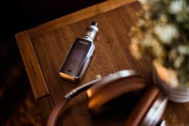 A vape device rests on a table beside a pair of headphones, suggesting a relaxed atmosphere for music and vaping.