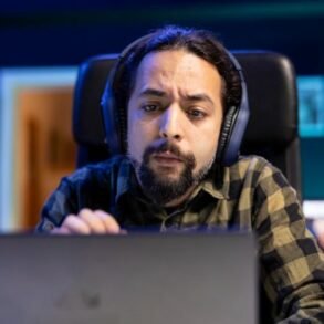 A man with headphones sits at a desk, focused on his laptop, engaging with AARP Games.