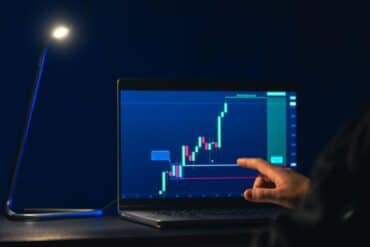 A person working on a laptop displaying a stock chart related to Biitland.com stablecoins.