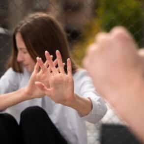 A woman sitting on a fence, making a fist, symbolizing strength and resilience in the context of foster care abuse.