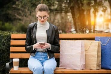 A woman sits on a bench with shopping bags, reflecting how online shopping has transformed daily habits.