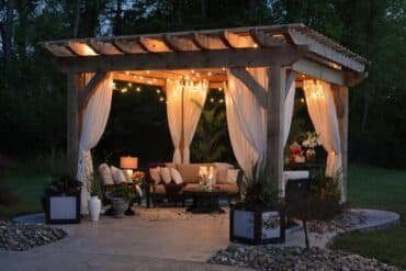 A beautifully lit gazebo adorned with flowing curtains, creating a cozy and inviting atmosphere.