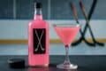 A pink drink labeled Pink Whitney with a hockey stick blurred in the background.