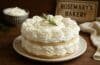 A delicious whipped cream cake topped with fresh rosemary, served on a white plate from Rosemary’s Bakery.