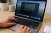 A person typing on a Mac laptop, focused on their work with a clear screen in front of them.