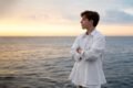 A young man in a white shirt stands at the ocean's edge, reflecting on therapeutic hobbies for a stress-free mind.