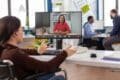 A woman in a wheelchair video chatting on a computer, engaging with others through a virtual meeting platform.