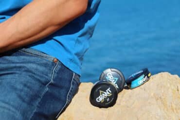 A man sits on a rock by the ocean, gazing at the waves under a clear blue sky.