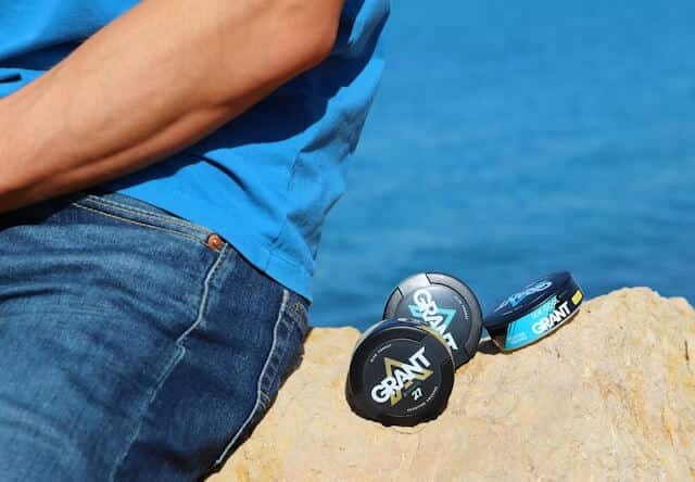A man sits on a rock by the ocean, gazing at the waves under a clear blue sky.
