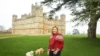 A woman in a red sweater and jeans stands with two dogs in front of Abbey Castle in London.