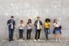 A diverse group of people smiles in front of a wall decorated with various social media icons.