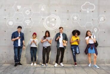 A diverse group of people smiles in front of a wall decorated with various social media icons.