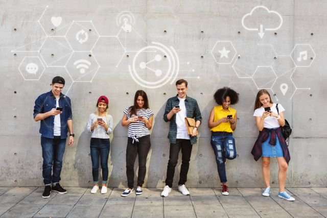 A diverse group of people smiles in front of a wall decorated with various social media icons.