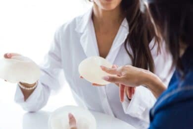 Breast implants alongside a breast cancer awareness ribbon, highlighting the connection between the two topics.