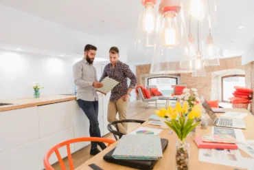 Two men standing in an office with a table and chairs, discussing lighting to enhance the space's appearance.